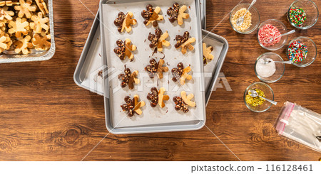 Creating snowflake-shaped cutout sugar cookies, dipped in chocolate, and adorned with crushed pecan nuts, elegantly presented on parchment. 116128461