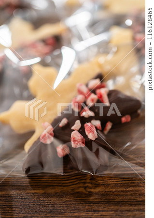 Carefully packaging Christmas cutout cookies, half-dipped in chocolate and presented in clear cellophane wrapping, perfect for festive gifting. 116128465