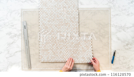 In the process of mounting peel and stick mosaic tiles onto a foam board, perfect for enhancing a food photography studio's aesthetic. 116128570