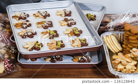 Carefully packaging Christmas cutout cookies, half-dipped in chocolate and presented in clear cellophane wrapping, perfect for festive gifting. 116128643
