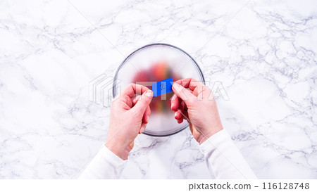 Flat lay. Strawberries, freshly washed and dried, are neatly stored in a glass bowl lined with a paper towel and securely covered with plastic wrap to maintain freshness. 116128748