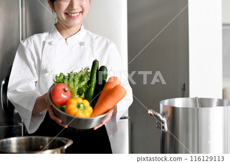 Young Asian female chef holding lots of vegetables 116129113