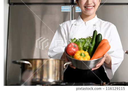 Young Asian female chef holding lots of vegetables 116129115