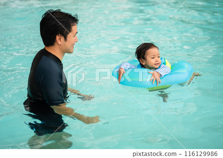 happy father with toddler baby girl playing in an inflatable ring in swimming pool 116129986