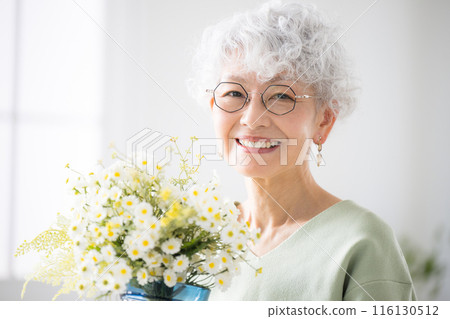 Senior woman holding flowers in her room, gardening and flower hobbies, looking at camera 116130512