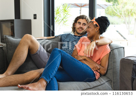 A diverse couple is relaxing together on a gray sofa at home A diverse couple is relaxing together on a gray sofa at home 116130653