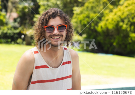 A young Caucasian man with curly hair smiles outdoors with copy space at home 116130678