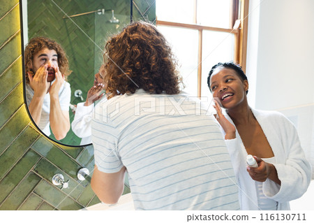 A diverse couple engages in their morning skincare routine in the bathroom at home 116130711