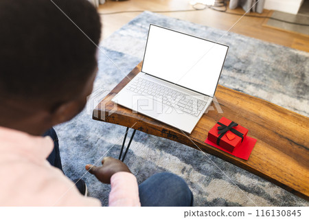 African American man on a video call with gift, looking at laptop with copy space 116130845