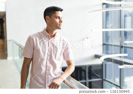 A young biracial man leaning on railing, looking to side in a modern business office with copy space 116130945