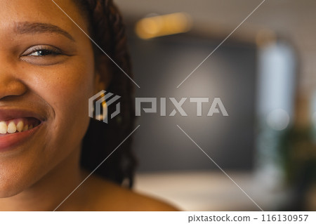Young biracial woman smiling, wearing gold hoop earrings in a modern business office with copy space 116130957