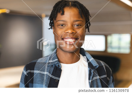 African American man standing, wearing plaid shirt, smiling at camera in a modern business office African American man standing, wearing plaid shirt, smiling at camera in a modern business office 116130978