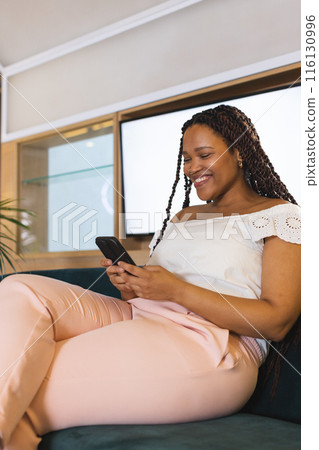 Biracial young woman sitting in a modern business office, using a smartphone 116130996