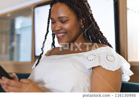 A young biracial woman with braided hair smiling at her phone A young biracial woman with braided hair smiling at her phone 116130998
