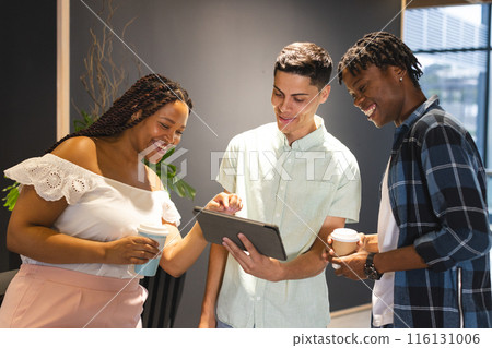 A diverse group of colleagues sharing a tablet and laughing together in a modern business office A diverse group of colleagues sharing a tablet and laughing together in a modern business office 116131006