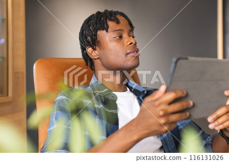 African American man holding tablet, looking at screen in a modern business office 116131026