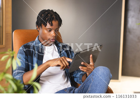 A young African American male using a tablet while sitting in a modern business office A young African American male using a tablet while sitting in a modern business office 116131033