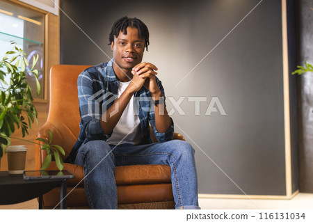 African American man sitting in a modern business office, hands clasped, looking at camera African American man sitting in a modern business office, hands clasped, looking at camera 116131034
