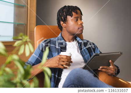 African American man holding coffee, looking at tablet in a modern business office African American man holding coffee, looking at tablet in a modern business office 116131037