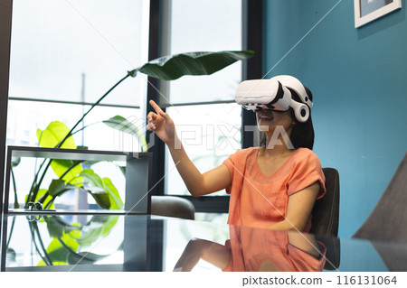 A young Asian woman wearing VR headset is pointing at something in a modern business office A young Asian woman wearing VR headset is pointing at something in a modern business office 116131064