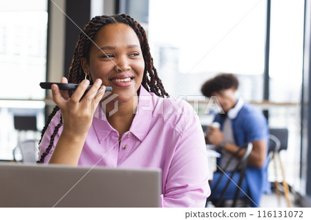 Young biracial woman talking on smartphone, working on laptop in a modern business office 116131072
