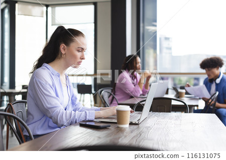 Caucasian woman typing on laptop in a modern business office, biracial woman and man talking 116131075