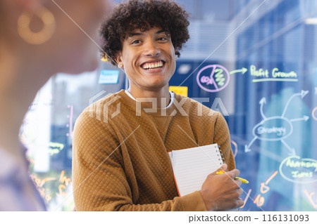 A young biracial male holding notepad, discussing ideas in a modern business office 116131093