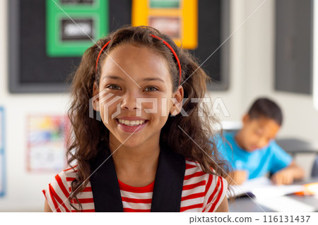 In school, young biracial female student smiling, wearing a striped shirt in classroom 116131437