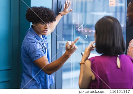 A diverse group of young adults discussing in front of a glass wall in a modern business office A diverse group of young adults discussing in front of a glass wall in a modern business office 116131517