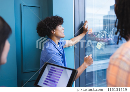 A diverse group of young adults is brainstorming with sticky notes in a modern business office 116131519