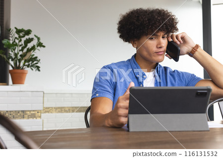 Young biracial man talking on phone, looking at tablet 116131532