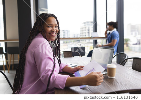 Biracial woman with braided hair is holding VR graphs, smiling, in a modern business office 116131540