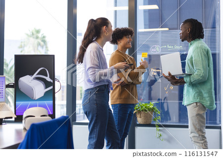 A diverse group of young colleagues discussing in office, holding papers and laptop 116131547