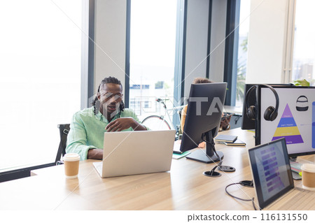 African American man with braided hair working on a laptop in a modern business office African American man with braided hair working on a laptop in a modern business office 116131550