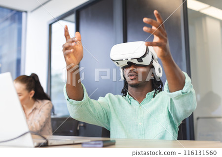 African American man wearing virtual reality headset, gesturing in a modern business office African American man wearing virtual reality headset, gesturing in a modern business office 116131560