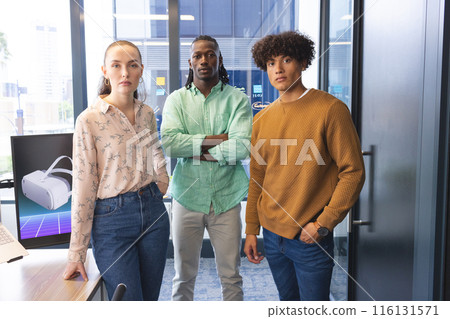 Diverse team standing in office, looking serious Diverse team standing in office, looking serious 116131571