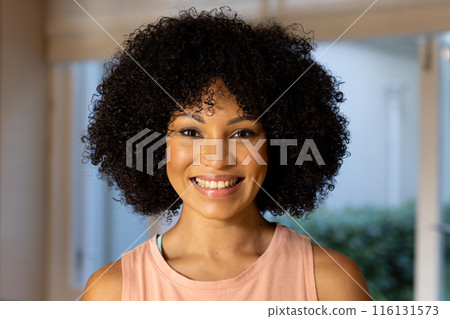 Biracial young woman with curly black hair smiling at camera at home Biracial young woman with curly black hair smiling at camera at home 116131573