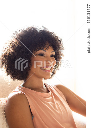Biracial young woman sitting at home, looking away, smiling gently 116131577