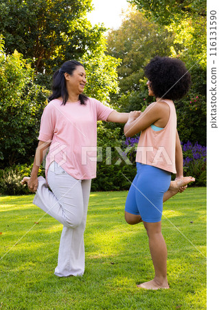 Mature biracial woman helping young biracial woman stretching in garden at home Mature biracial woman helping young biracial woman stretching in garden at home 116131590