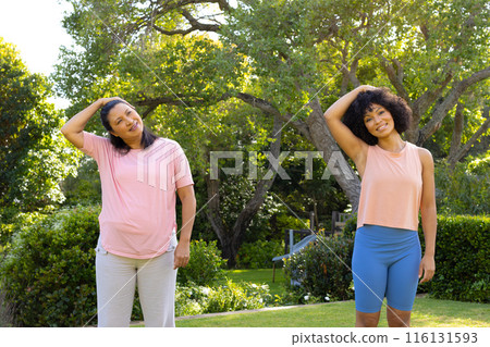 Mature biracial woman and young biracial woman stretching in park at home 116131593