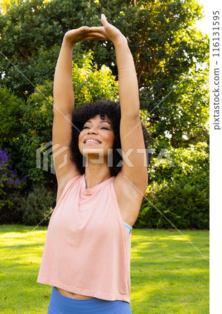 Biracial young woman stretching arms in garden at home 116131595