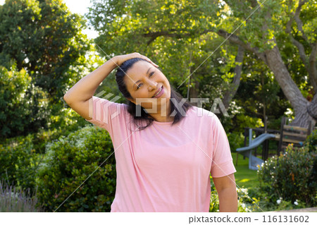 Mature biracial woman standing outside, stretching neck and smiling at home Mature biracial woman standing outside, stretching neck and smiling at home 116131602