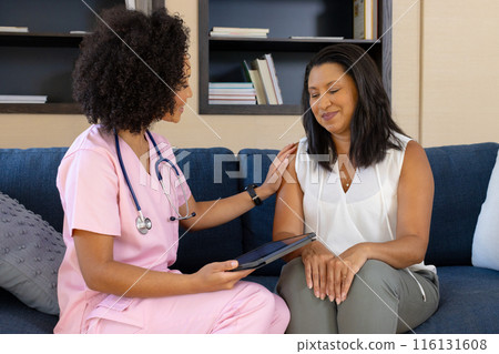 Biracial nurse holding tablet is talking to mature biracial woman at home 116131608