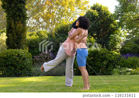 Mature biracial woman hugging young adult daughter in garden at home 116131611