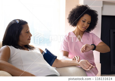 Mature biracial woman checking blood pressure at home, young nurse assisting 116131614