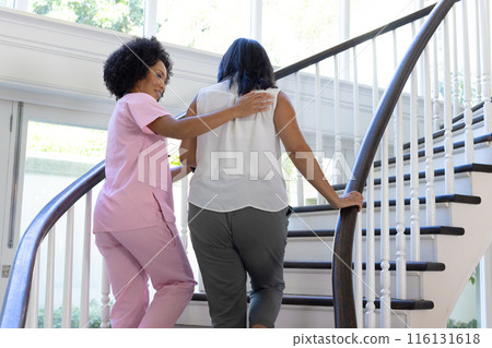 Mature biracial nurse assisting biracial woman up stairs at home Mature biracial nurse assisting biracial woman up stairs at home 116131618