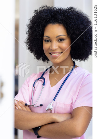 Biracial nurse standing with arms crossed, wearing scrubs at home Biracial nurse standing with arms crossed, wearing scrubs at home 116131628