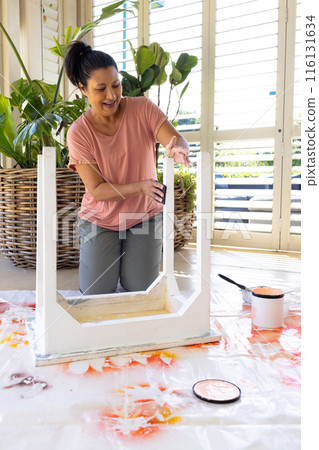 Mature biracial woman painting furniture at home in an upcycling project, wearing casual clothes 116131634