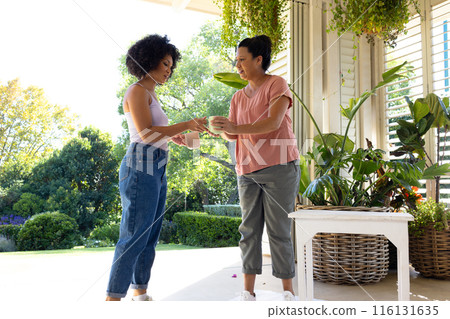 Biracial mother and adult daughter are drinking coffee outside at home 116131635