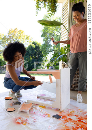 Mature biracial woman watching young biracial woman painting table at home for an upcycling project 116131639